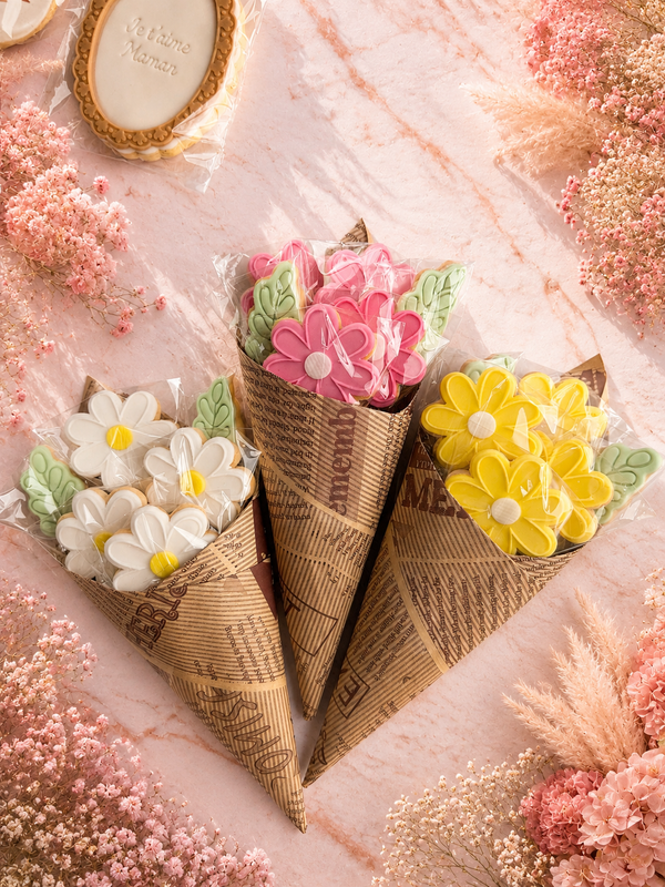 Bouquet de biscuits fleurs décorés en pâte à sucre rose, blanc et jaune avec feuilles vertes dans un emballage kraft
